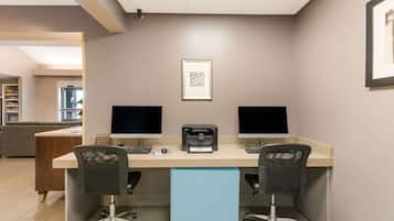 Un espacio de oficina moderno con dos escritorios, cada uno con un monitor, teclado y ratón. Hay una impresora en la pared y un cuadro enmarcado sobre los escritorios.