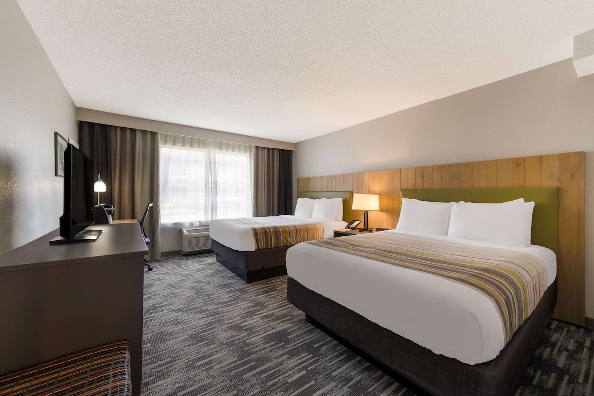 A hotel room with two beds, a desk, a TV, and a window with curtains.