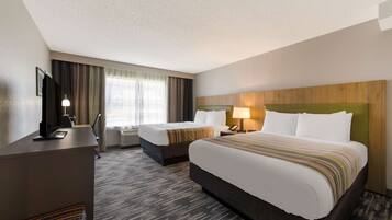 A hotel room with two beds, a desk, a TV, and a window with curtains.