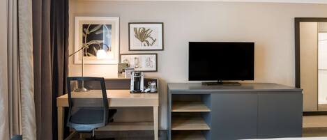 Habitación de hotel con cama, escritorio con silla, televisión y una obra de arte en la pared.