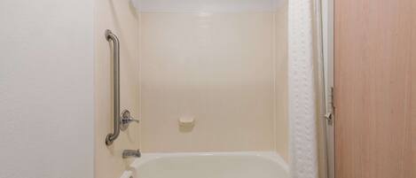 A bathroom with a bathtub, a handrail, and a shower curtain.