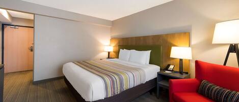 Una habitación de hotel con una cama, un sofá rojo, una mesita de noche con lámpara y una puerta de madera.