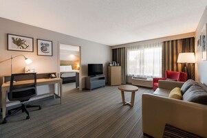 A hotel room with a desk, a television, a sofa, and a small round table.