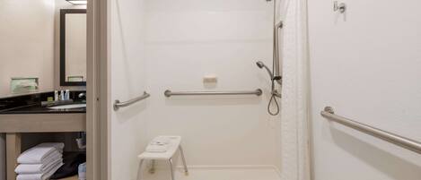A hotel bathroom with a walk-in shower, a small stool, a towel rack, and a mirror.