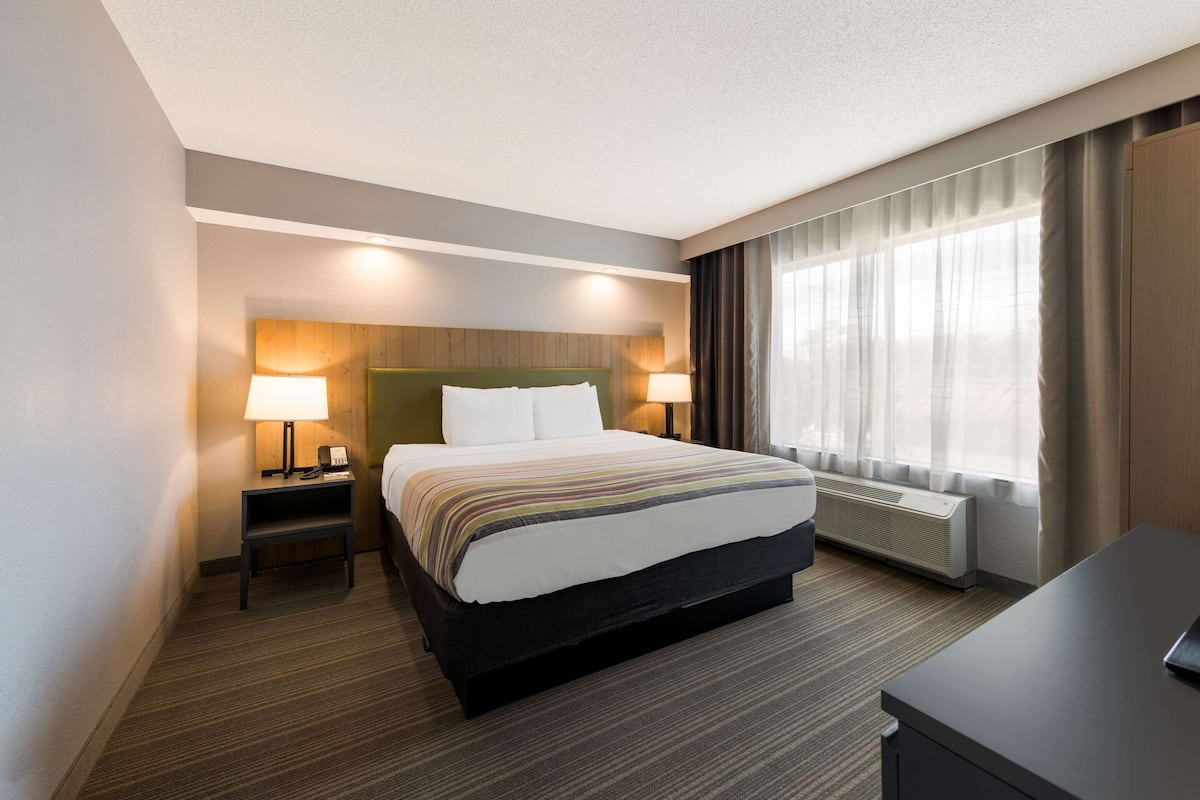 A hotel room with a large bed, two bedside lamps, a nightstand, a desk, and a window with curtains.