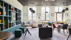 A modern lounge area with seating, a bookshelf, and large windows. - Holiday Inn Lincoln by IHG (Lincoln)