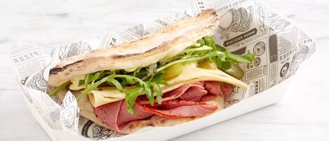 Un sandwich préparé avec du pain grillé, du fromage, des légumes verts et de la viande, servi sur une feuille de papier imprimée avec un motif de journal.