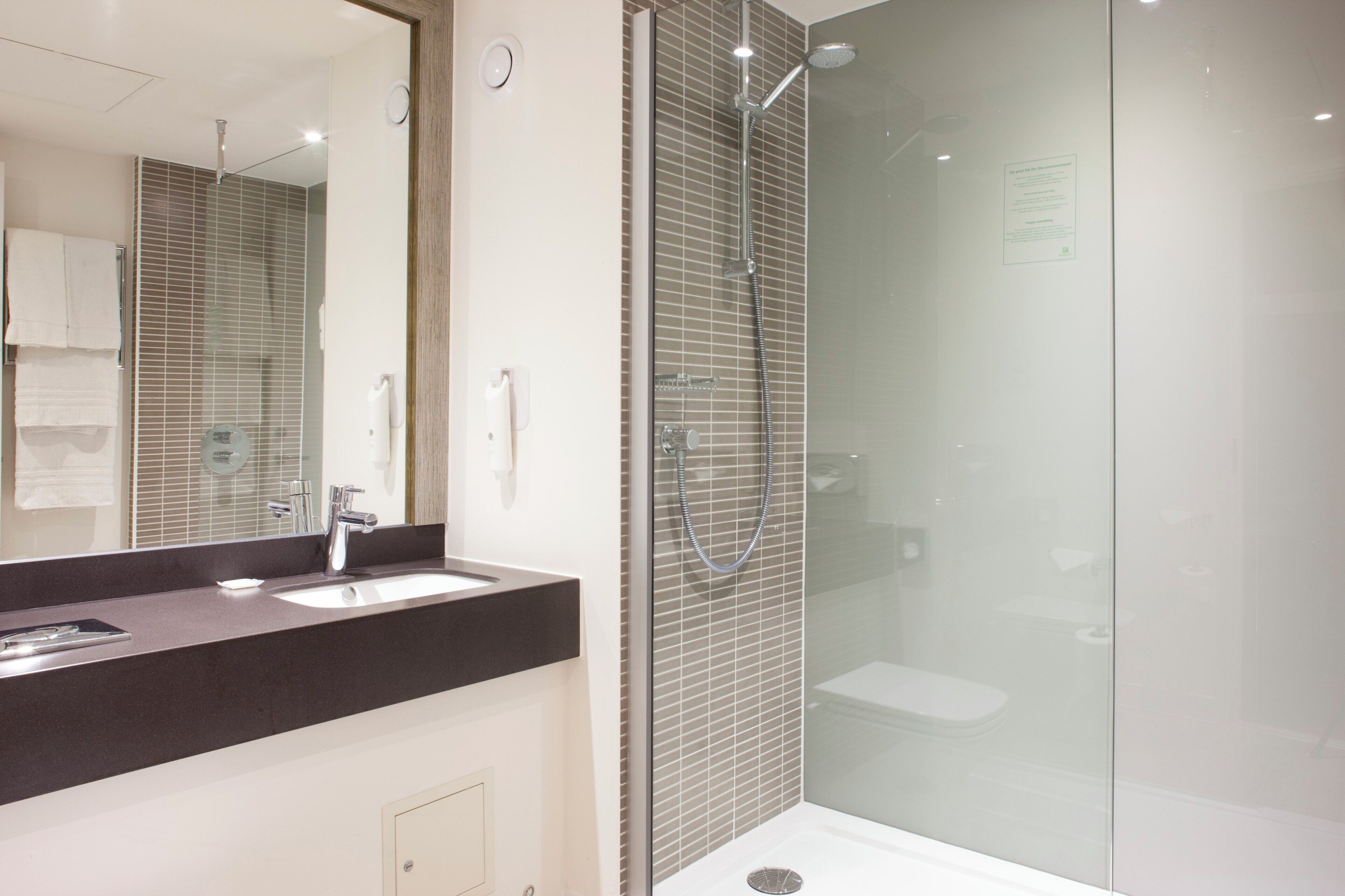 A modern bathroom with a glass-enclosed shower, a large mirror, and a dark countertop.