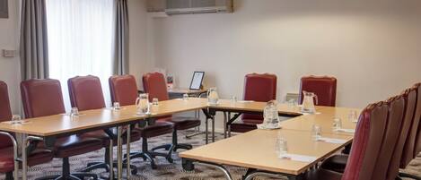 A conference room with a long table, red chairs, and a projector screen.