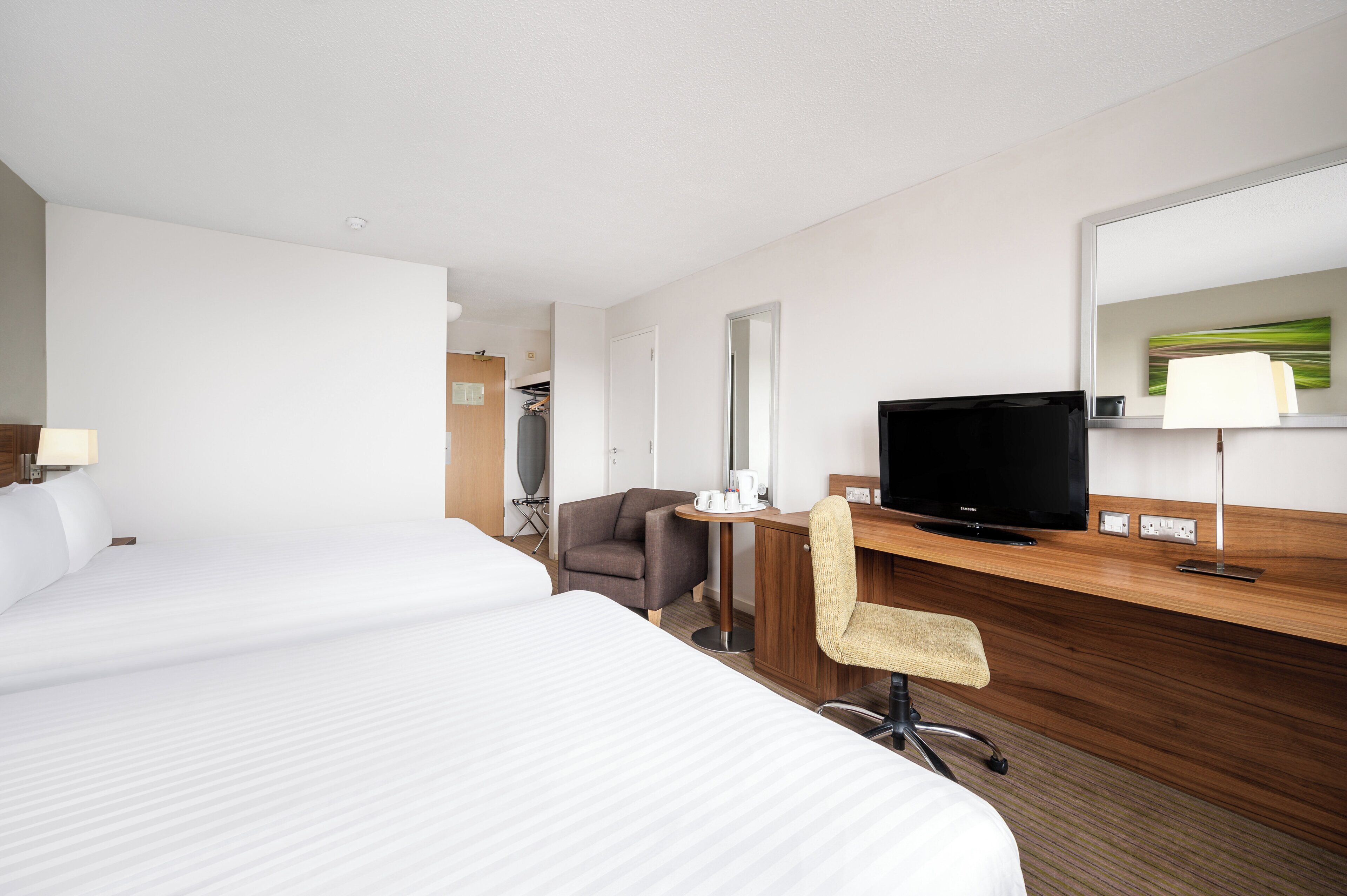 A hotel room with a bed, a desk with a television, a chair, and a mirror.