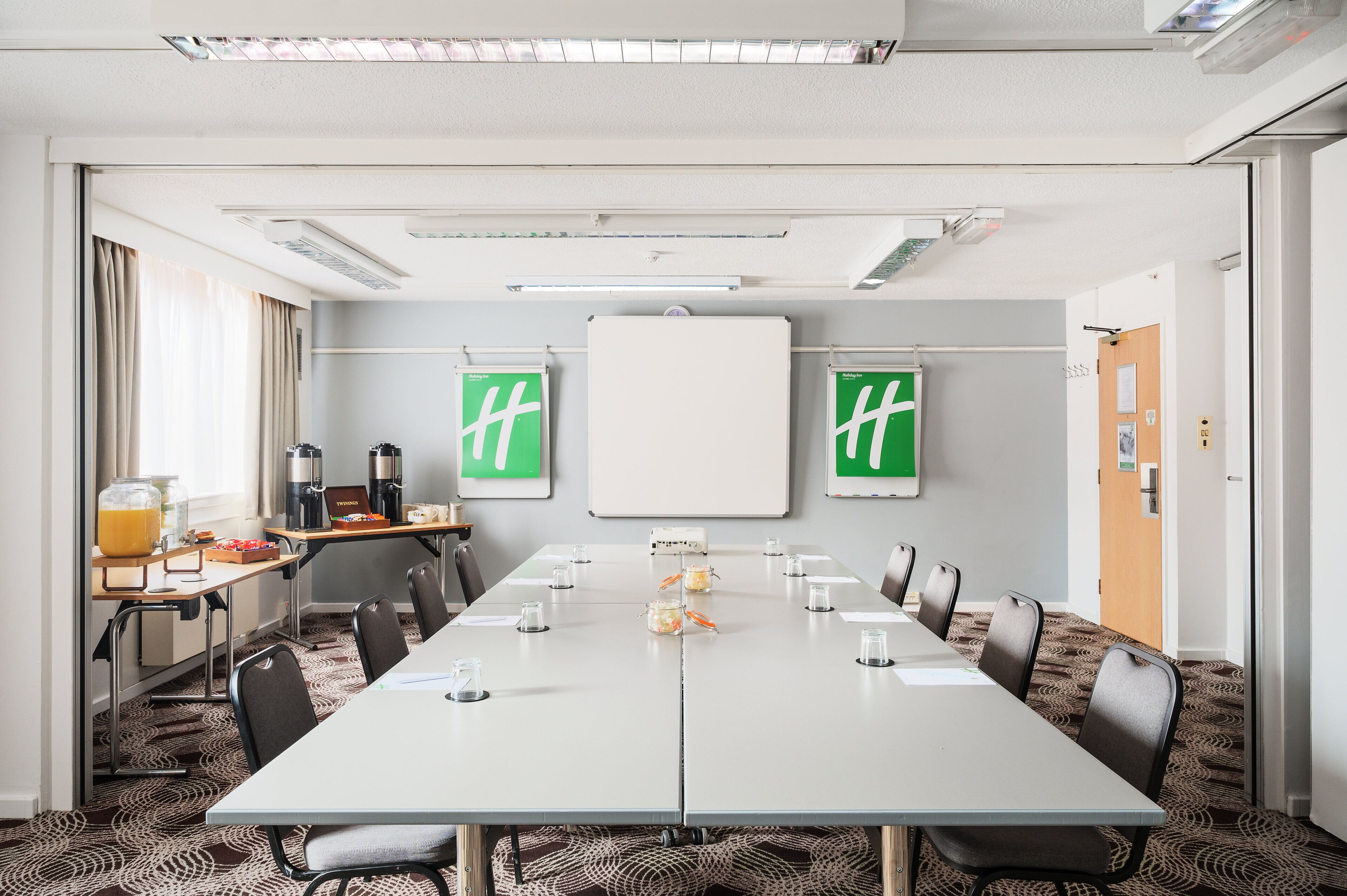 A conference room with a long table, chairs, a whiteboard, and two green signs with 'hh' on them.