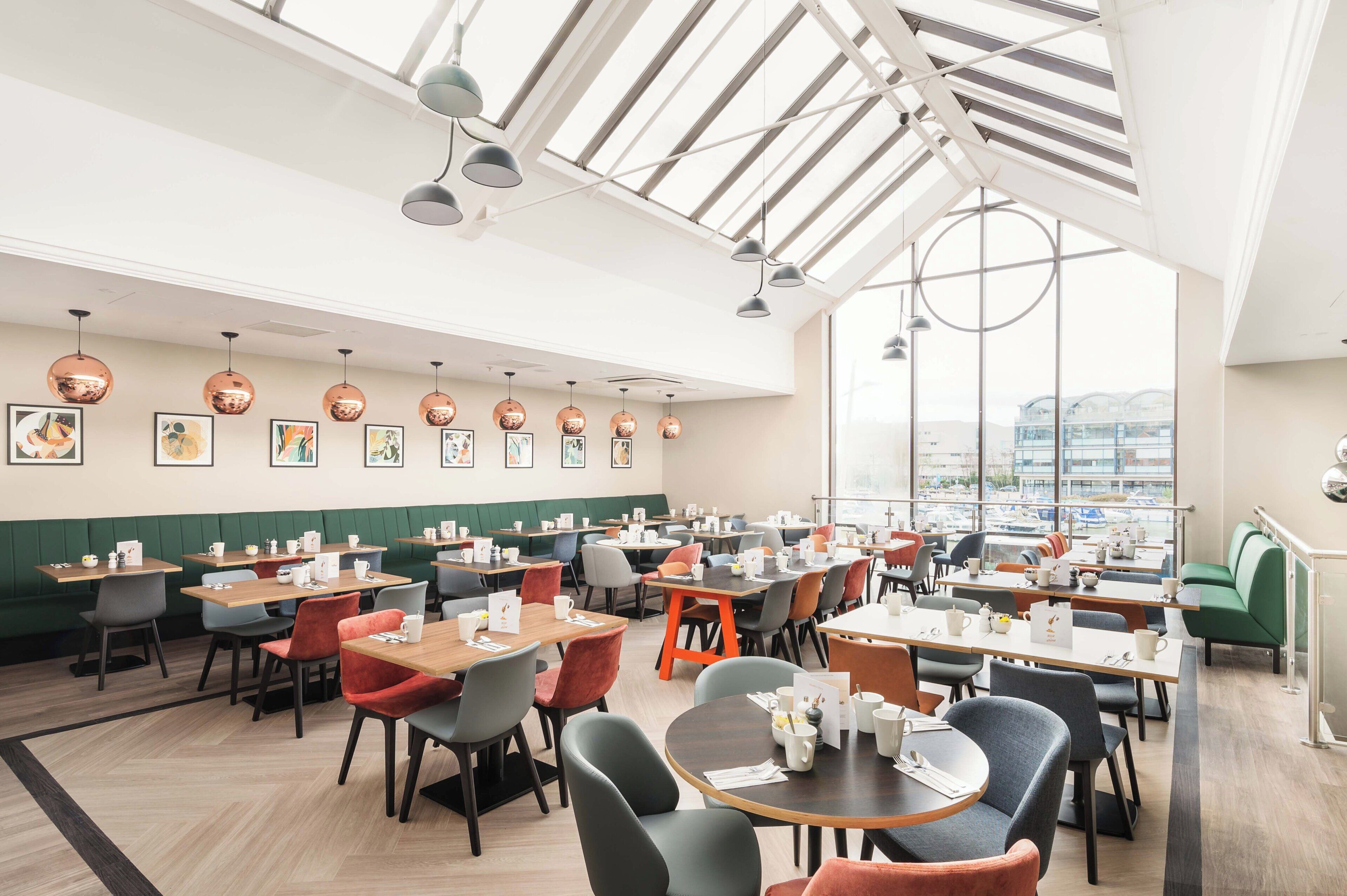 Un espace repas moderne doté de plusieurs tables et chaises, de grandes fenêtres et d’œuvres d’art accrochées aux murs.