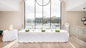A modern hotel room with a large window offering a city view, a round dining table set for a meal, and a decorative cake on a side table. - Holiday Inn Lincoln by IHG (Lincoln)