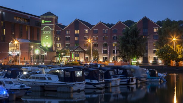 A marina with boats docked in front of a hotel with multiple buildings and a prominent tower. - Holiday Inn Lincoln by IHG (Lincoln)
