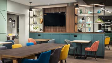 Un interior moderno con una mesa de comedor de madera, sillas coloridas, un televisor de pantalla plana y estantes con objetos decorativos.