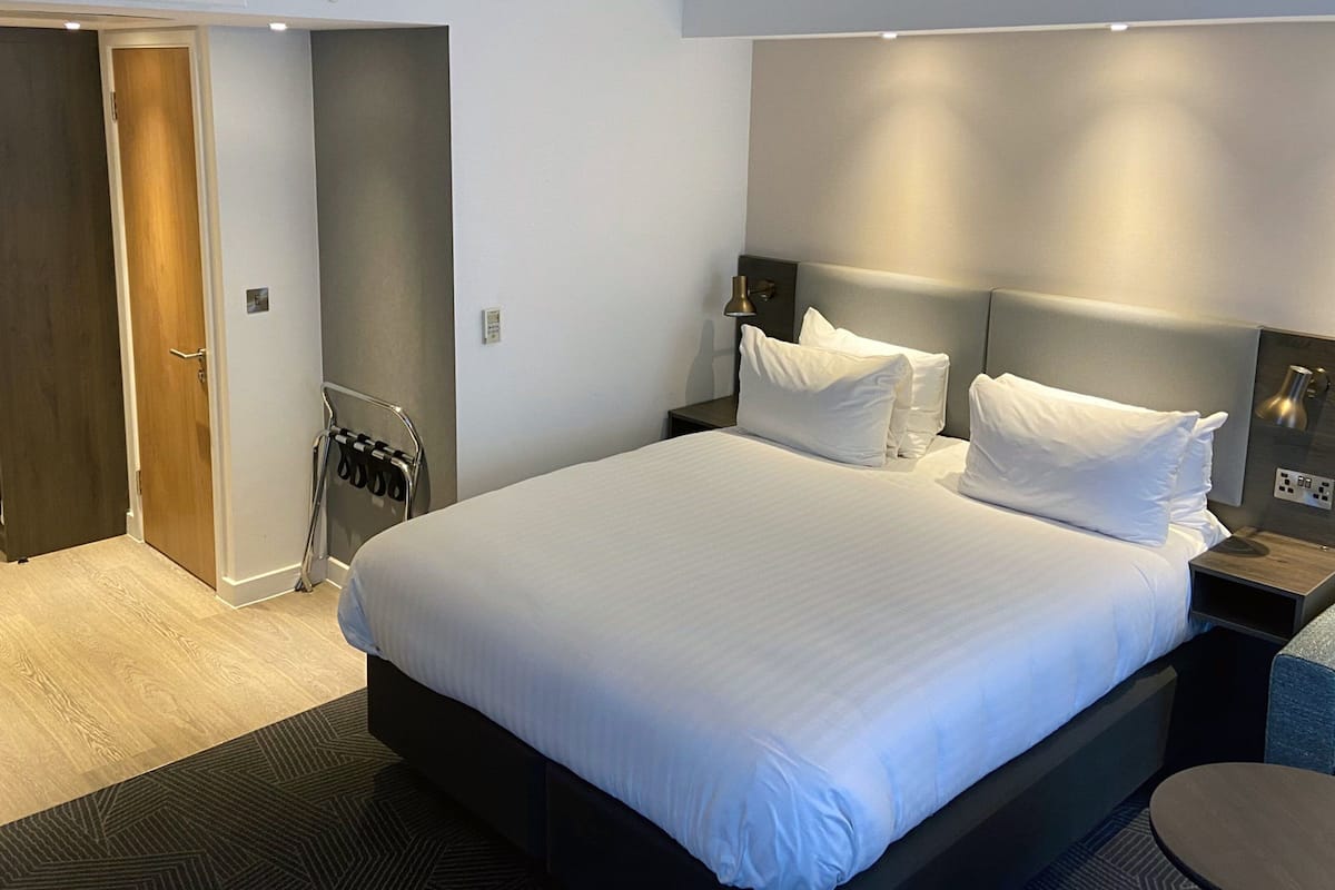 A hotel room with a large bed, a bedside table, a lamp, and a seating area with a chair and table.
