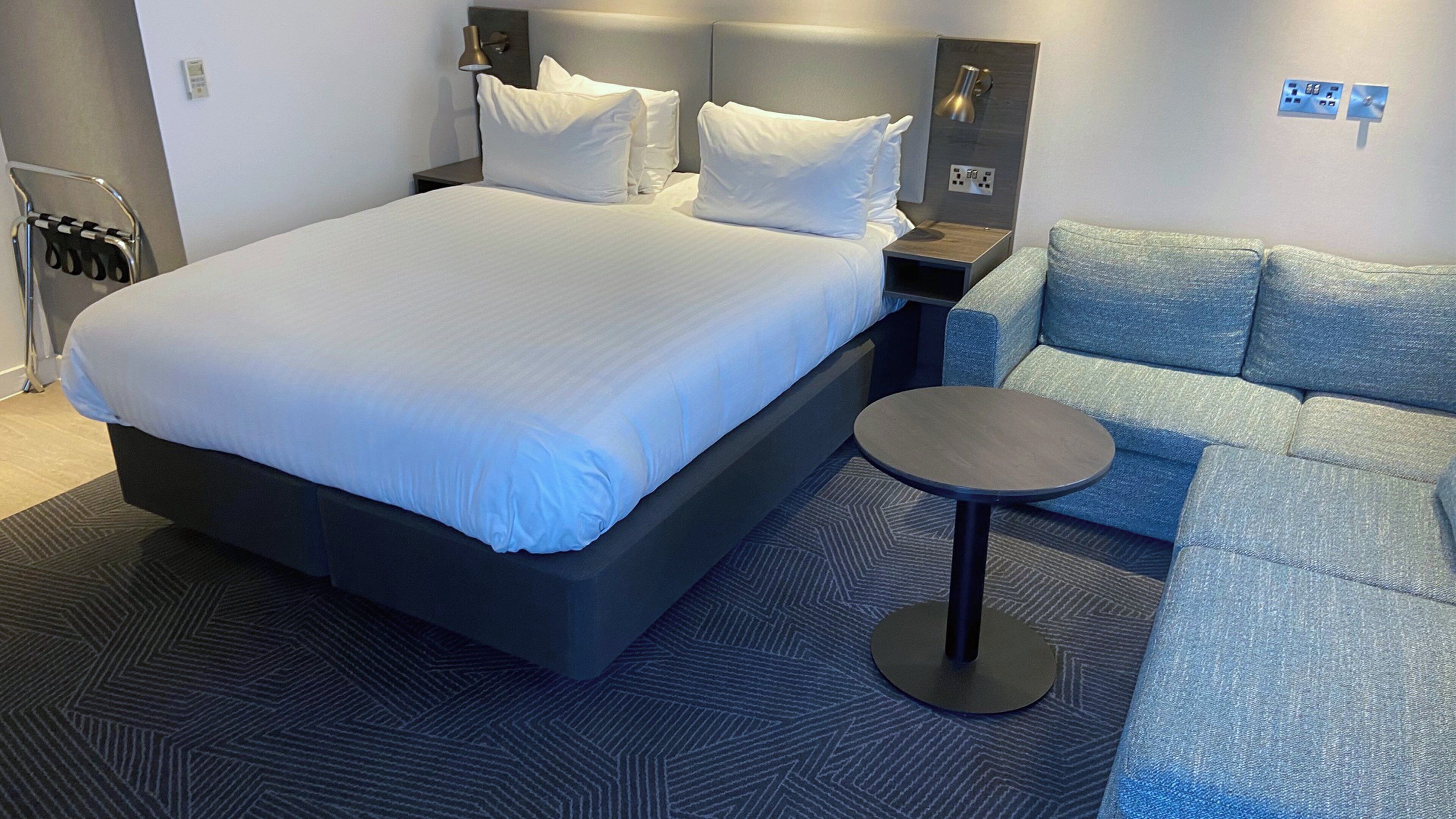 A hotel room with a large bed, a small round table, a sofa, and a chair.