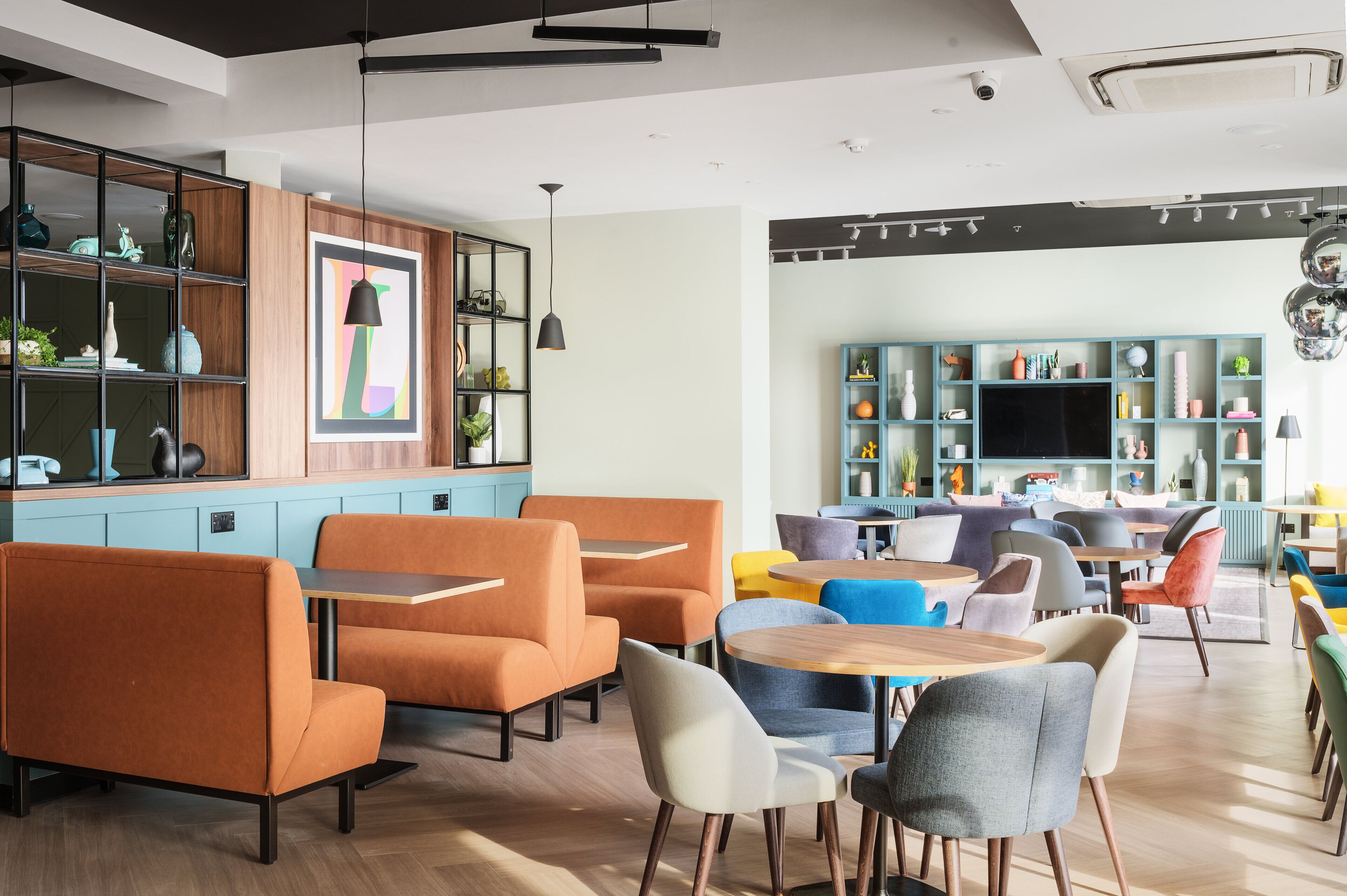 Un caffè moderno con sedute arancioni, scaffali in legno e un grande schermo televisivo.