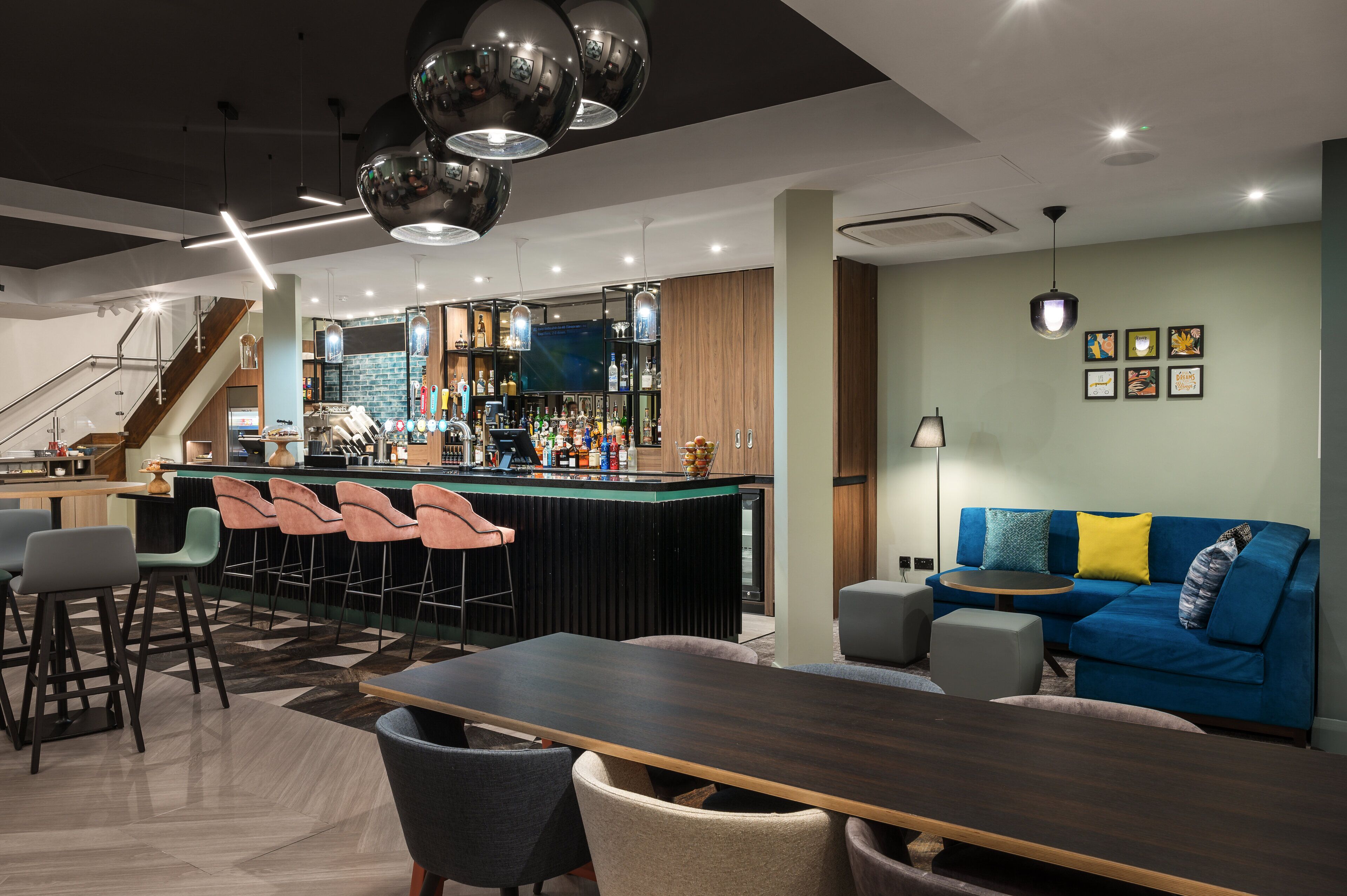 Un bar moderno con barra, taburetes y una variedad de botellas. Hay un sofá y una mesa de comedor con sillas al frente.