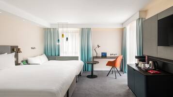 A hotel room with a bed, a desk with a chair, a television, and a coffee machine.