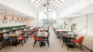 A spacious dining area with multiple tables and chairs, a high ceiling with skylights, and artwork on the walls. - Holiday Inn Lincoln by IHG (Lincoln)