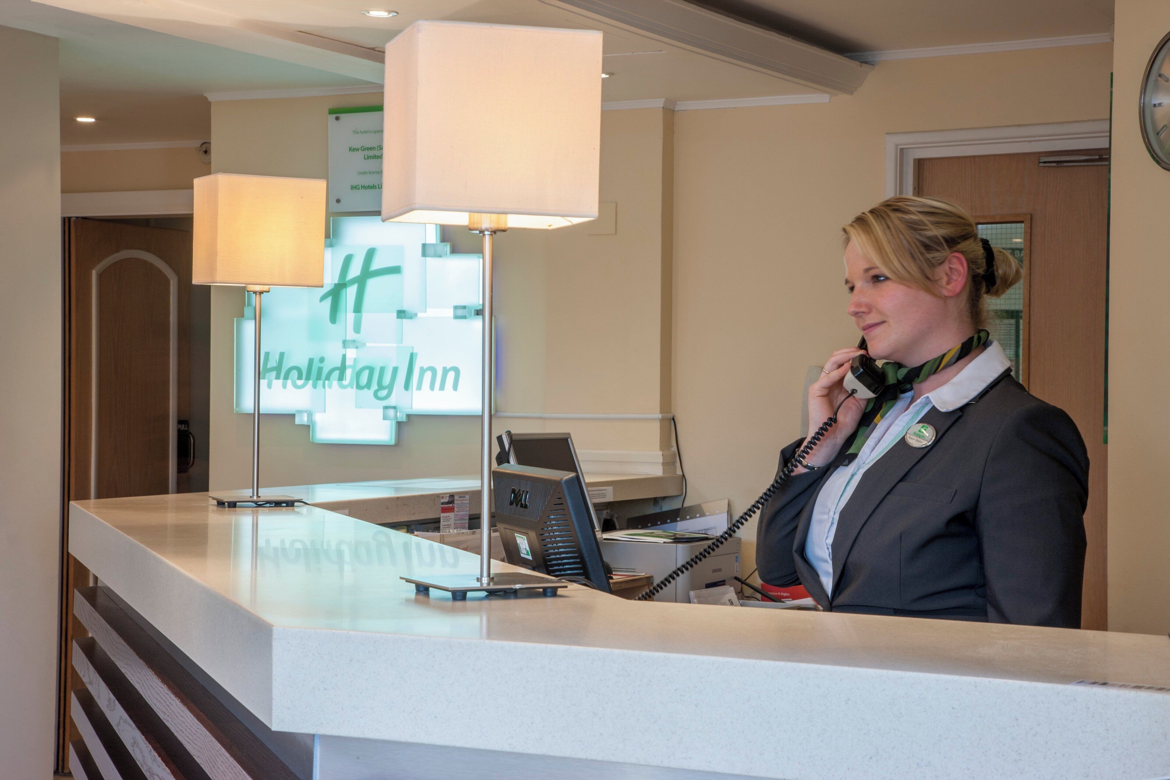 Ein Hotelrezeptionstresen mit einem Computer, einem Telefon und einem Schild mit dem Hotelnamen.