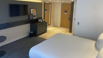 A hotel room with a bed, a desk, a TV, and a door.