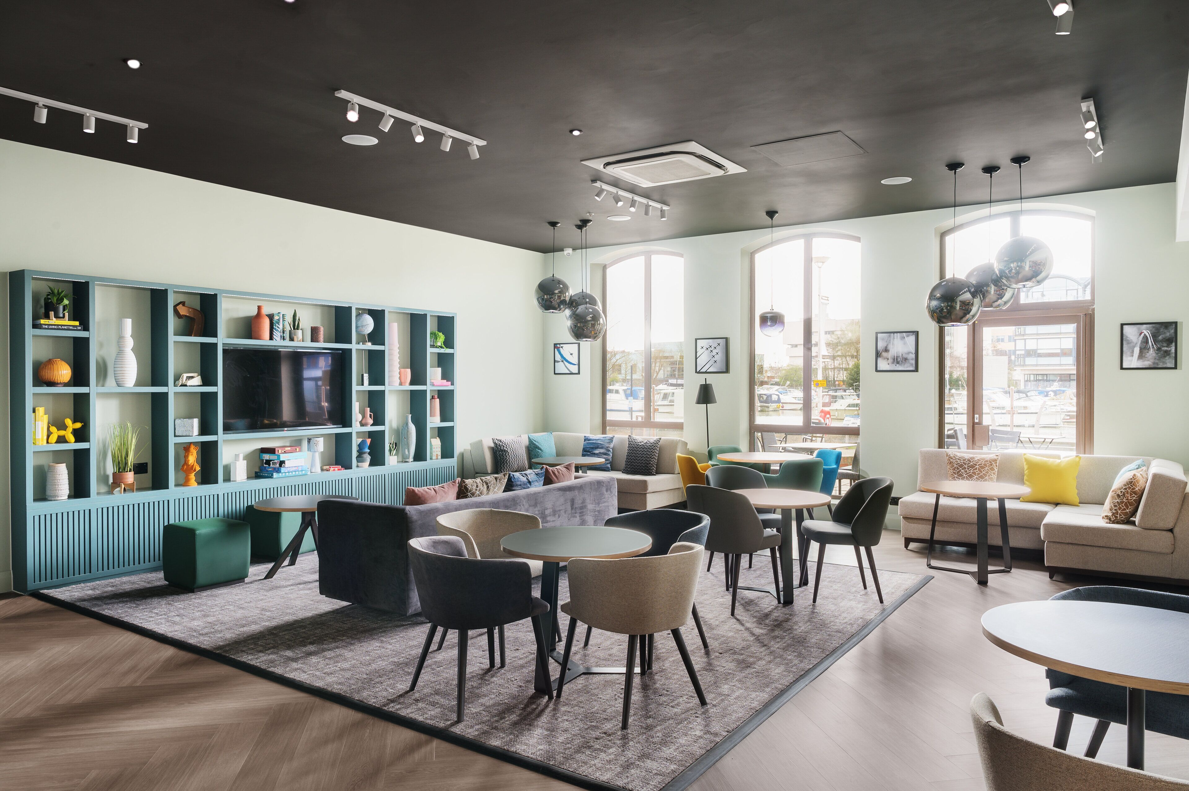 A modern lounge area with seating, a bookshelf, and large windows.