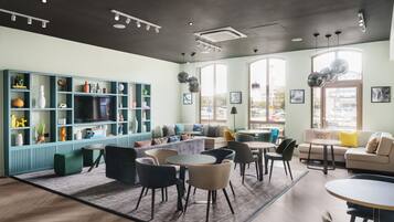 A modern lounge area with seating, a bookshelf, and large windows.