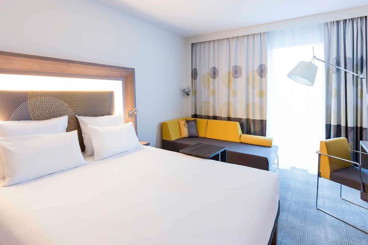 A hotel room with a large bed, a sofa, a small table, and a chair.