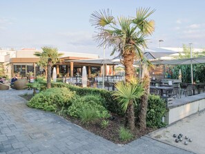Un patio al aire libre con disposición de asientos, palmeras y una estación de parrillada.