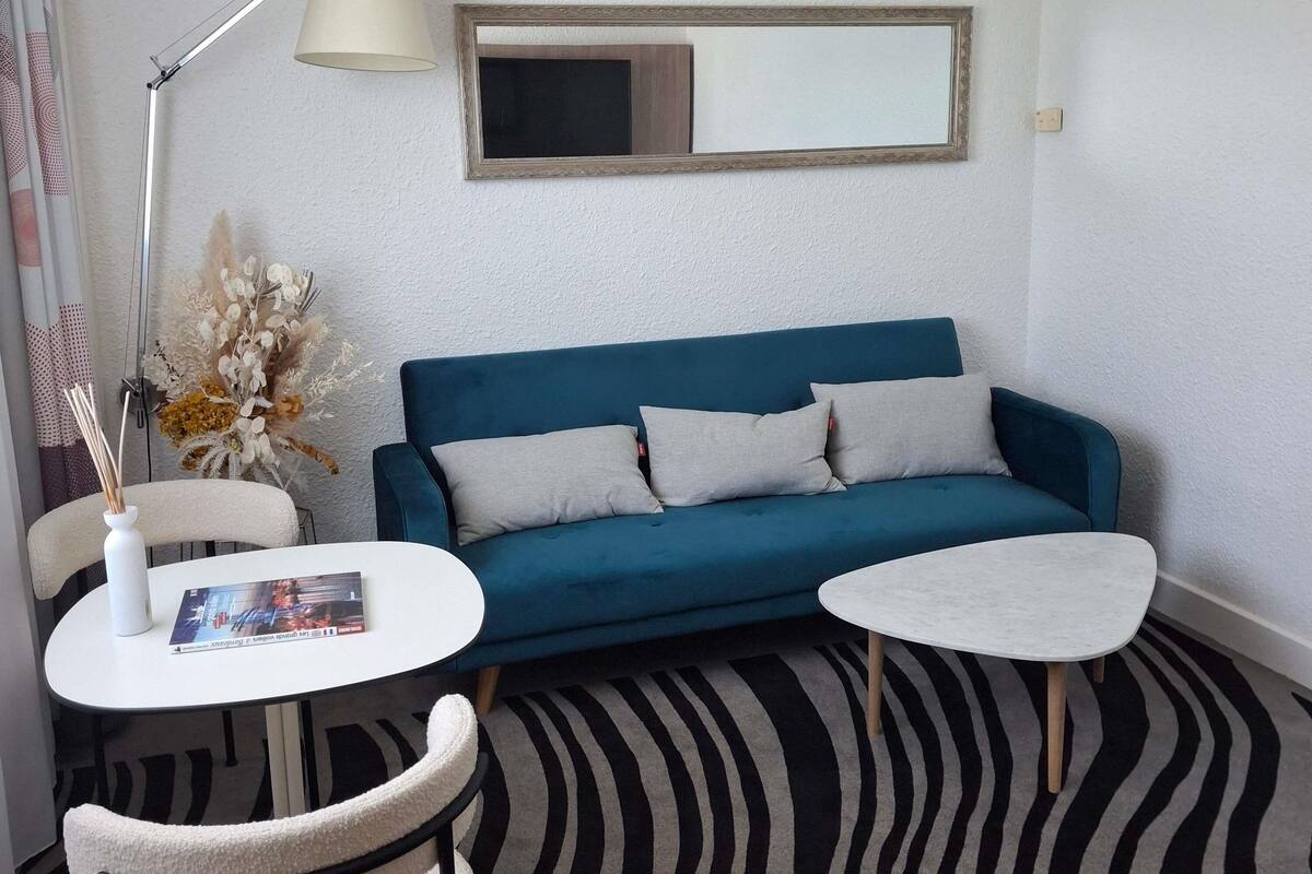 A room with a blue sofa, two white side tables, a lamp, a mirror, and a patterned carpet.