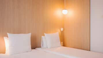 Una cama bien tendida con sábanas y almohadas blancas, cabecero de madera y una lámpara fijada a la pared.