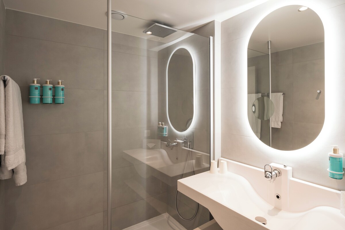 A modern bathroom with a glass-enclosed shower, a large mirror with integrated lighting, and a white sink.