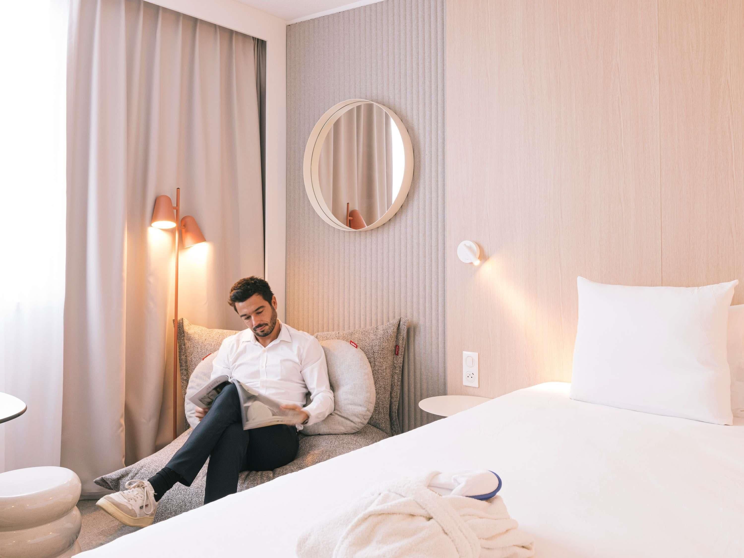 Habitación de hotel con una cama, una lámpara de noche, un espejo redondo, una almohada, una bata y una mesita de noche.
