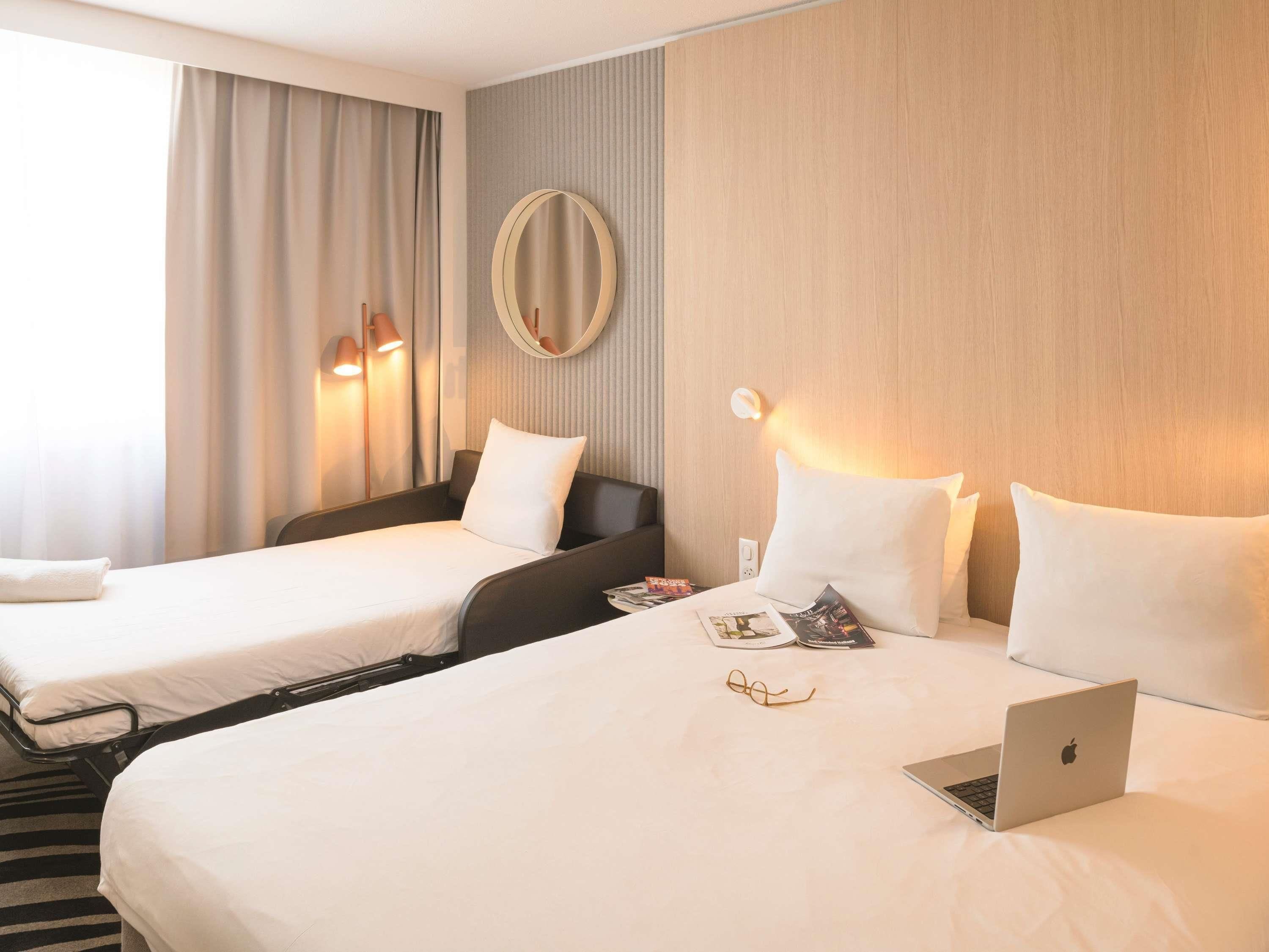 Habitación de hotel con dos camas, una laptop y una revista sobre la cama más grande.