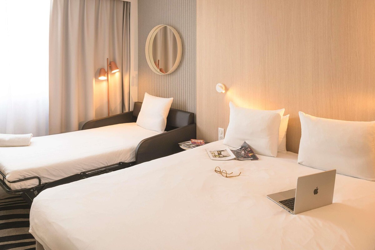 A hotel room with two beds, a laptop, and a magazine on the larger bed.