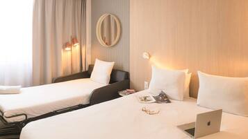 Habitación de hotel con dos camas, una laptop y una revista sobre la cama más grande.