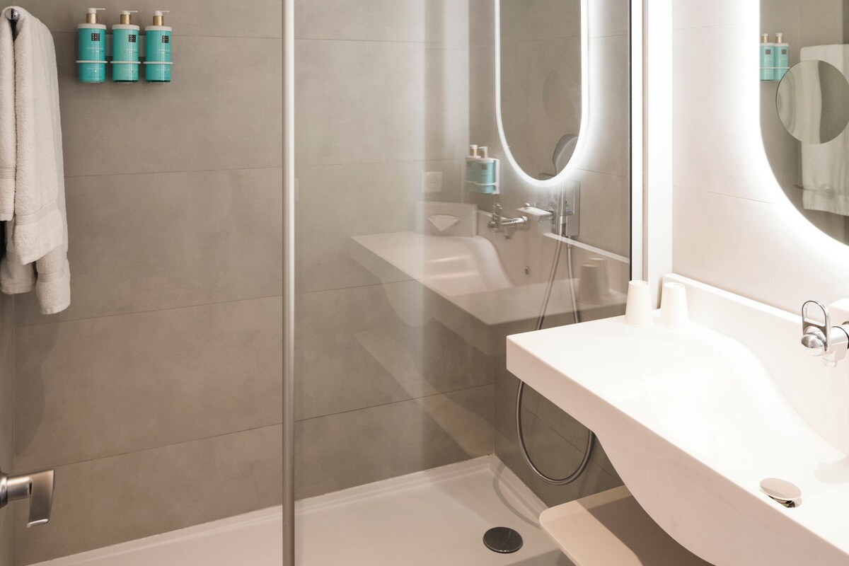 A modern bathroom with a glass shower enclosure, a white sink, and a large mirror.