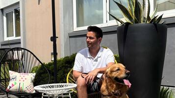 A man sitting on a chair with a dog beside him, a small table, and a large planter.