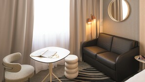 Habitación de hotel con una mesa redonda, un sofá, una silla, una pequeña mesa redonda y un espejo en la pared.