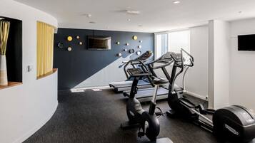 Une salle de sport moderne équipée de tapis de course, de vélos elliptiques et d’un téléviseur fixé au mur.
