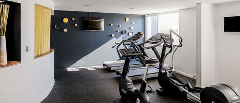 A modern gym with treadmills, ellipticals, and a wall-mounted TV.