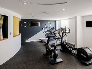 A modern gym with treadmills, ellipticals, and a wall-mounted TV. - Novotel Bordeaux Lac (Bordeaux)