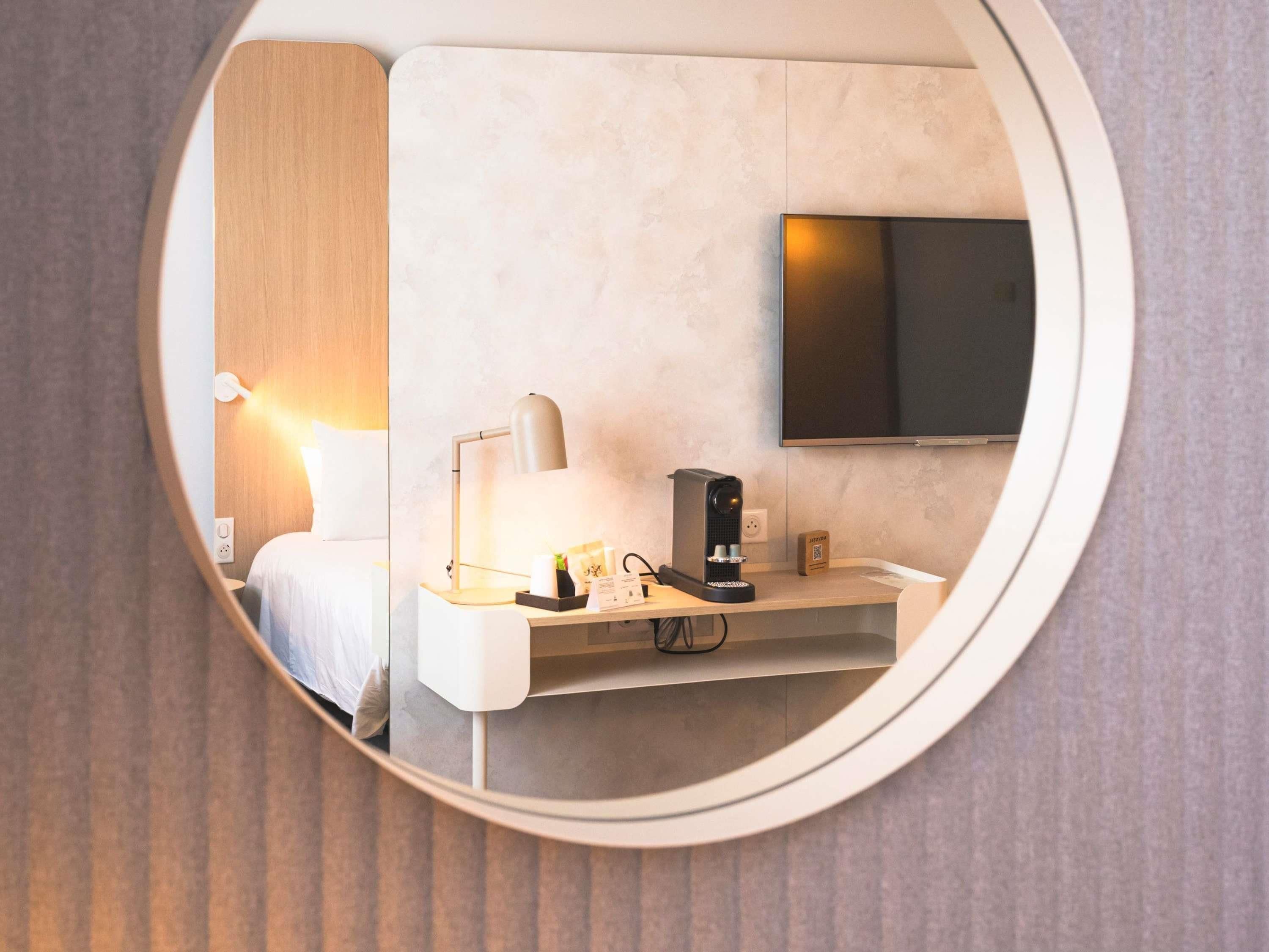 A hotel room with a bed, bedside lamp, desk with a coffee maker, and a mounted TV.
