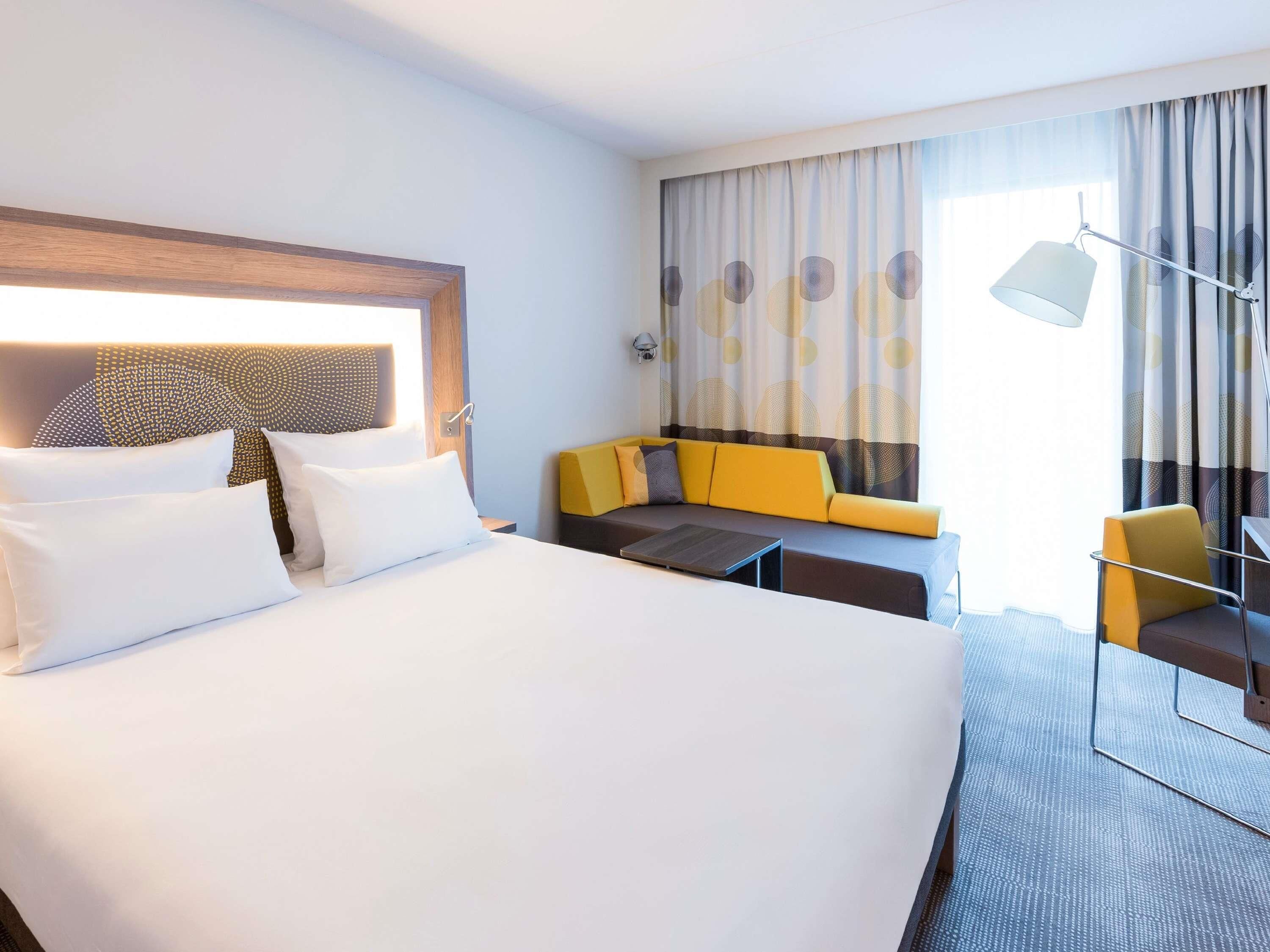 A hotel room with a large bed, a sofa, a small table, and a lamp.