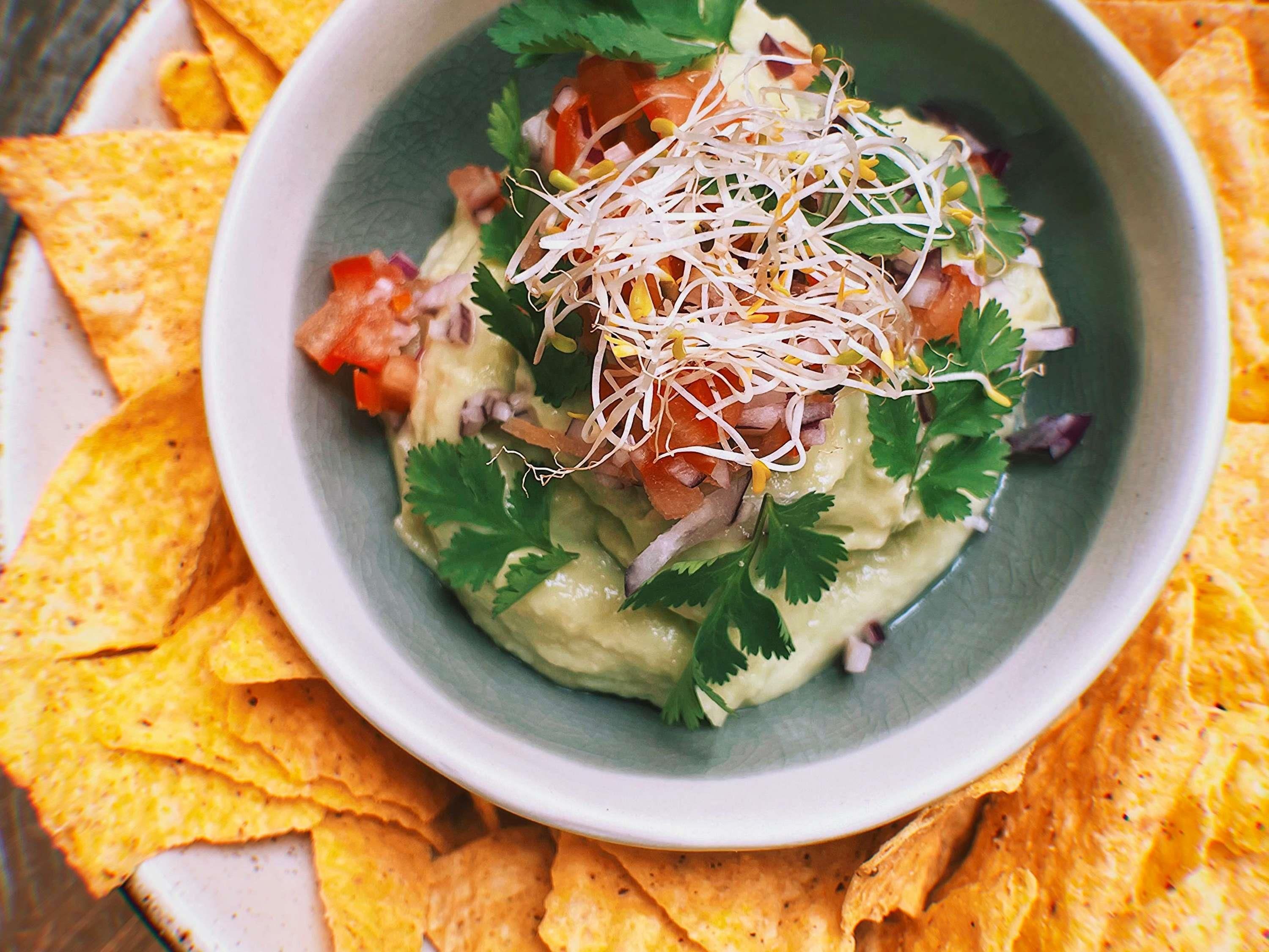 Un tazón de guacamole cubierto de brotes y cilantro, rodeado de totopos.
