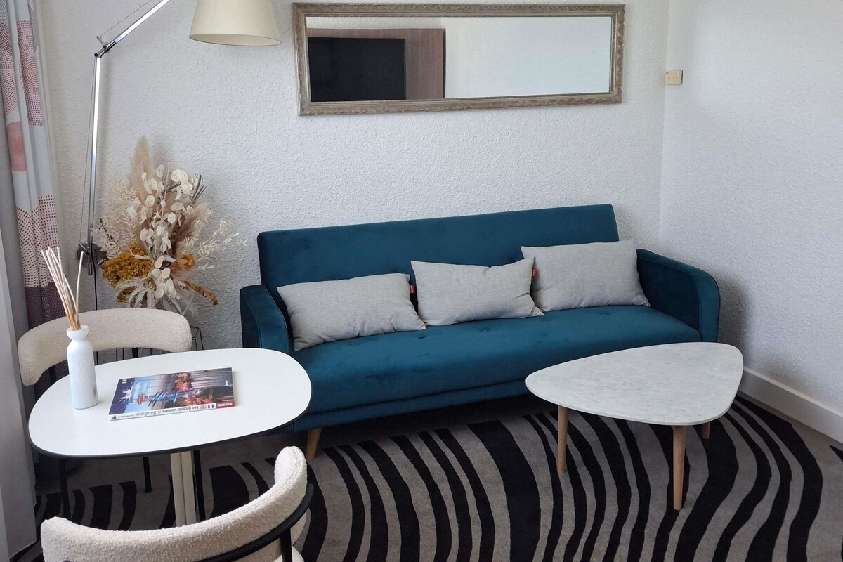 A room with a blue sofa, two white side tables, a lamp, a mirror, and a patterned carpet.