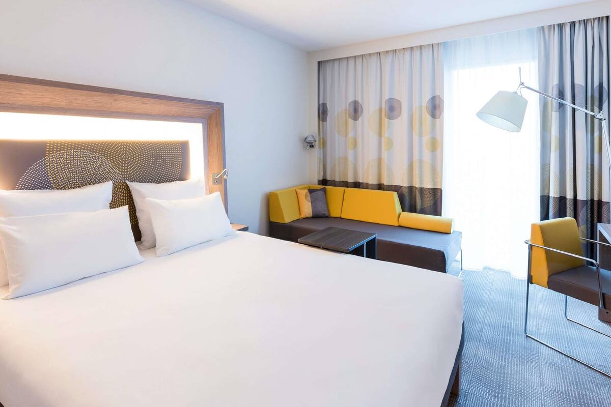 A hotel room with a large bed, a sofa, a small table, and a lamp.
