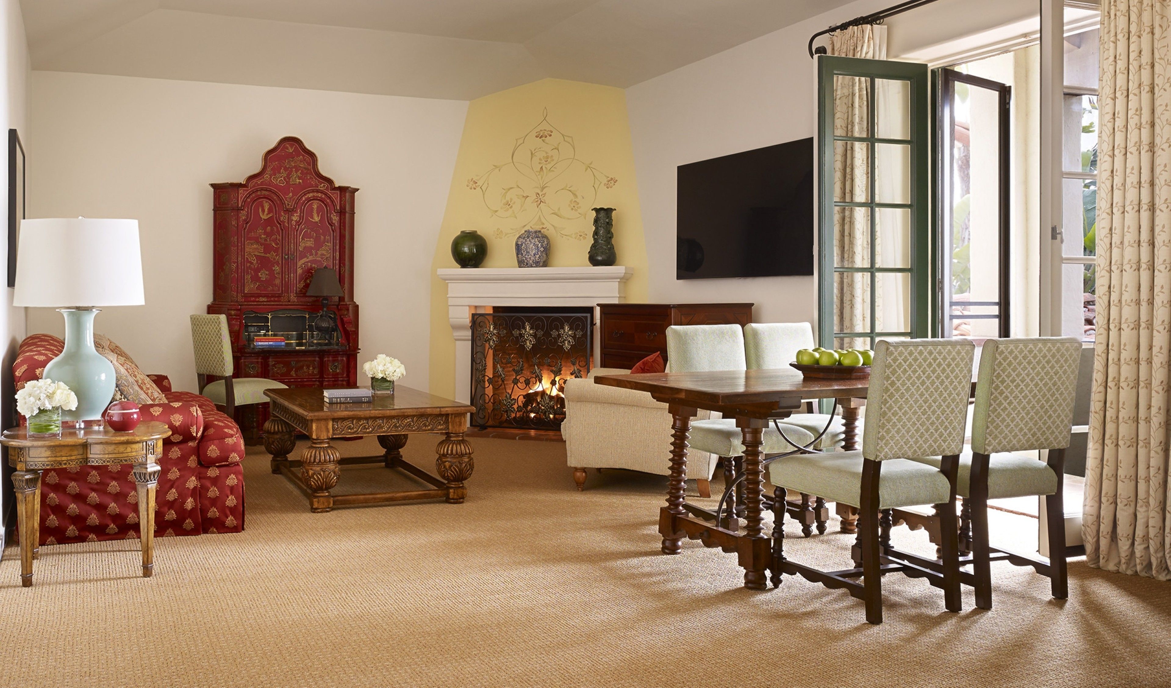 A traditional living room with a fireplace, a red cabinet, and a dining area with chairs and a table.